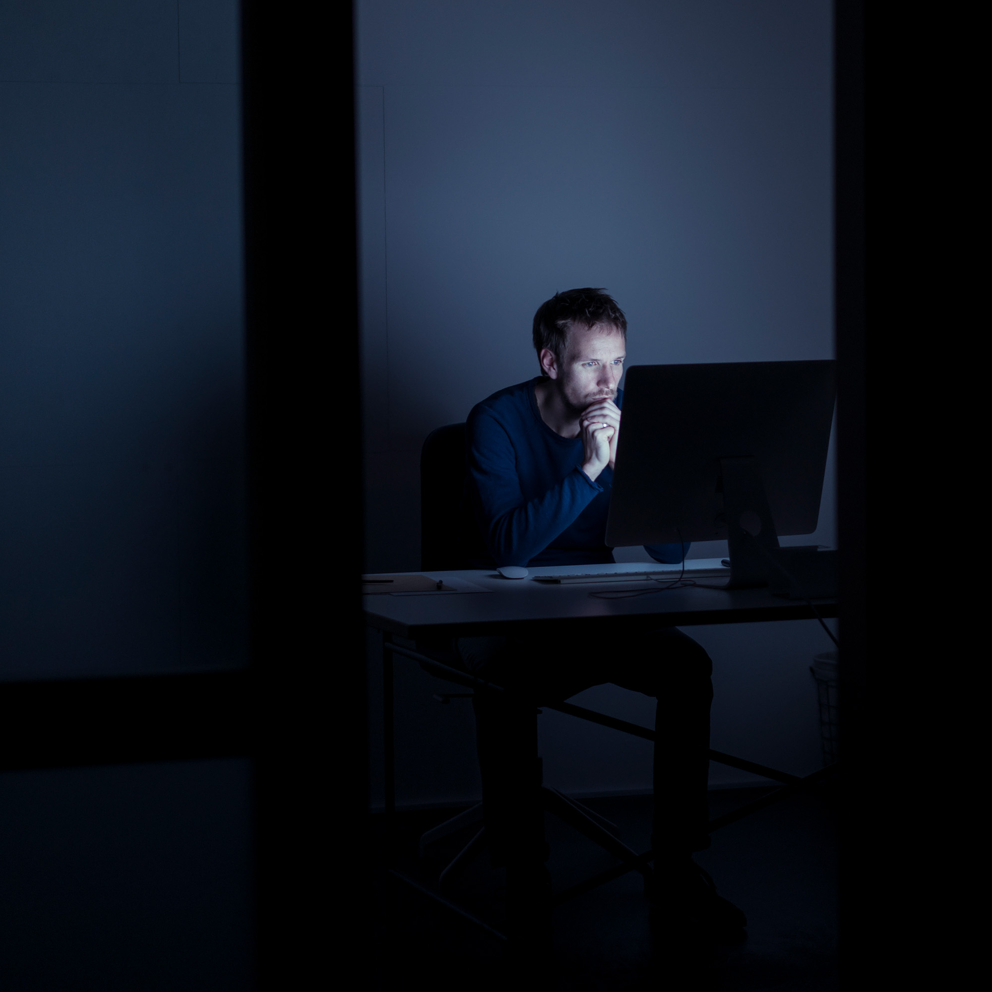 Mann sitzt im Dunkeln vor dem Computer und blauen Bildschirmlicht