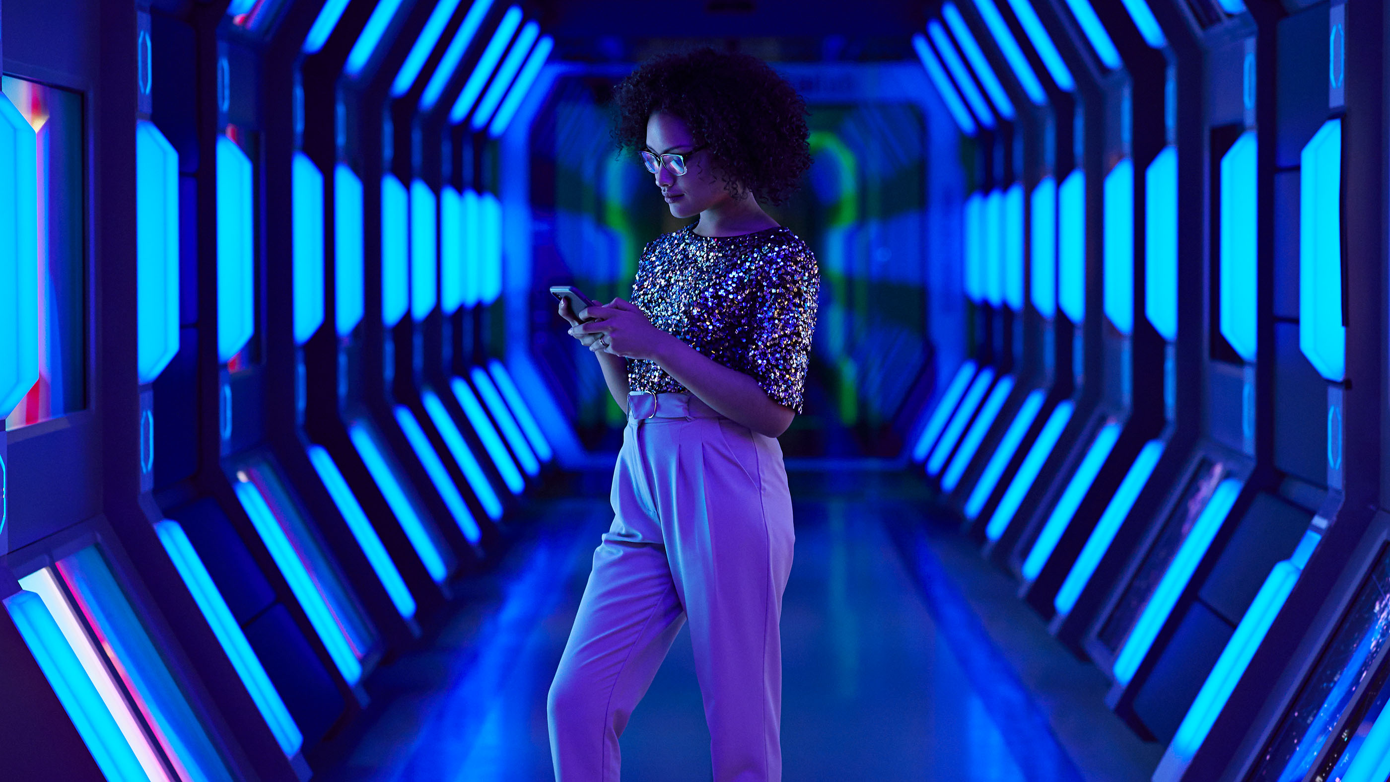 Junge Frau steht in blauem Lichttunnel und schaut auf ihr Handy